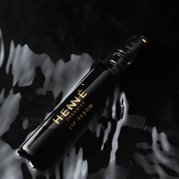 Henné Organics Luxury Lip Serum open lying flat on black watery surface