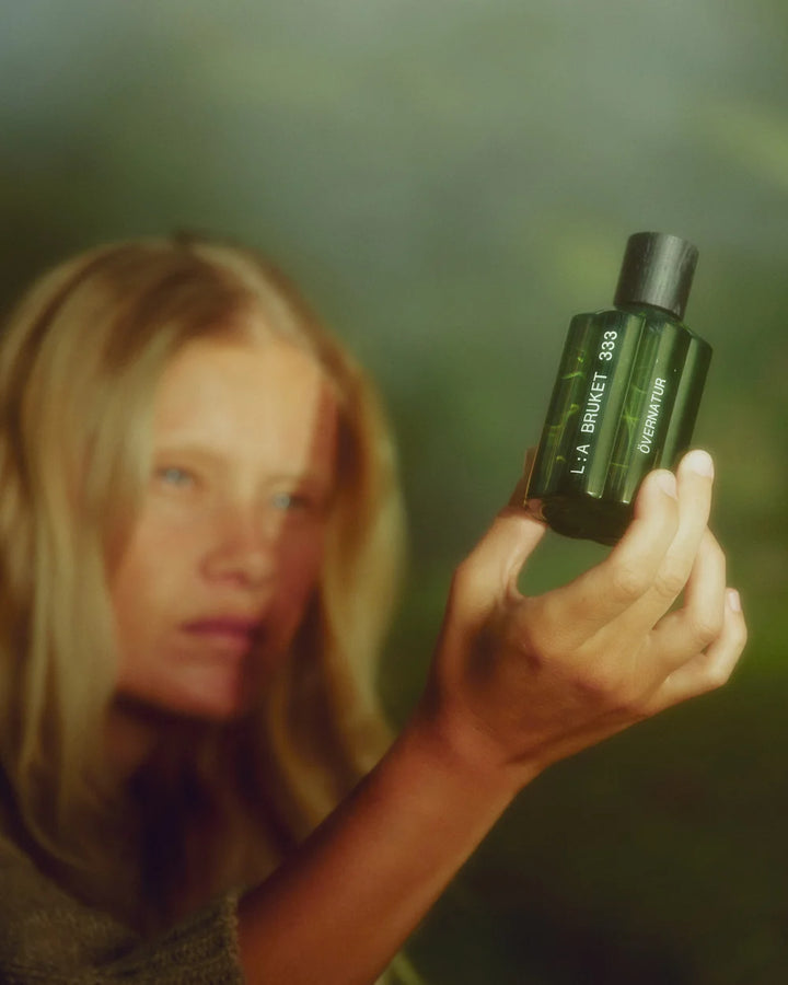 Frau mit langem blondem Haar hält den dunkelgrünen Övernatur Parfumflakon in der Hand