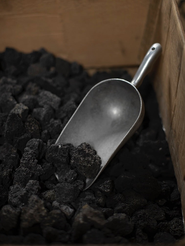 Schwarze Lavasteine in einer Metallschaufel für Mad et Len Pot Pourri Lava