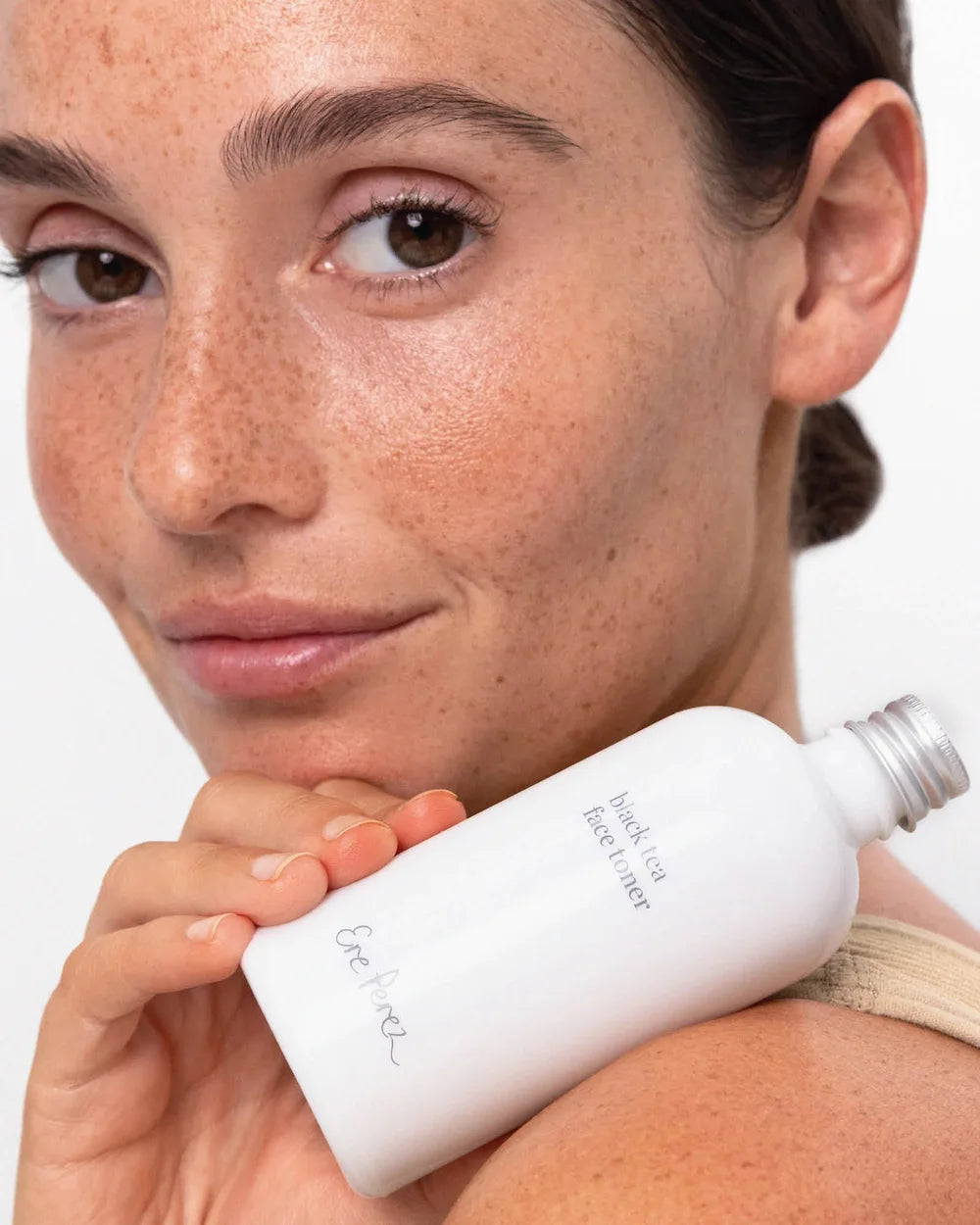 Model hält den Ere Perez Black Tea Face Toner an die Wange – Gesichtspflege für frische, hydratisierte Haut