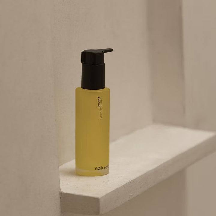 Naturallogic Inhabit Body Oil in gelber Glasflasche mit Pumpspender auf hellem Regal