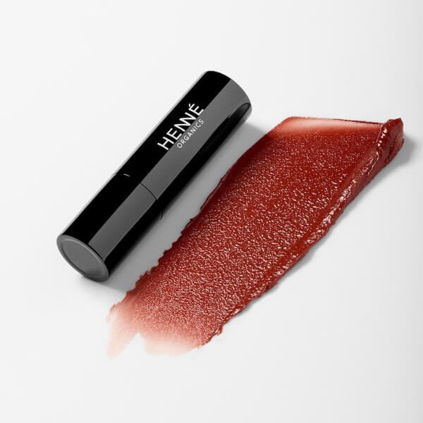 Henné Organics Luxury Lip Tint Intrigue tumbado sobre una superficie blanca con muestra